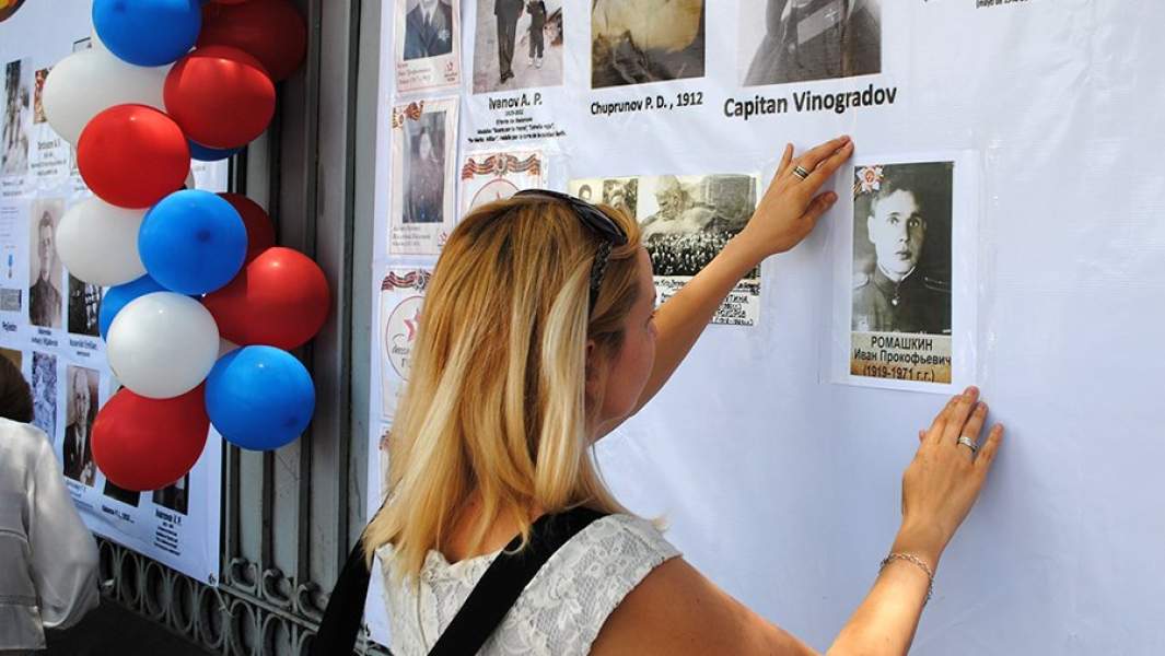 Участница акции «Бессмертный полк» клеит фотографию родственника на мероприятии в честь Дня Победы в Мехико