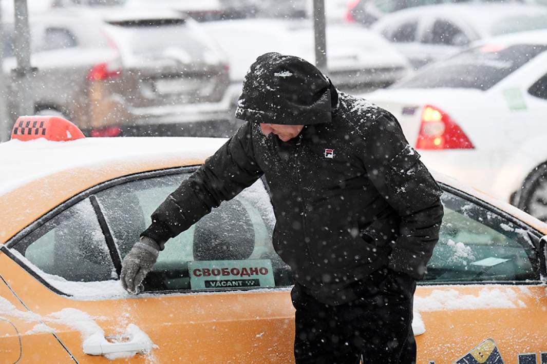Водитель такси очищает автомобиль от снега во время снегопада