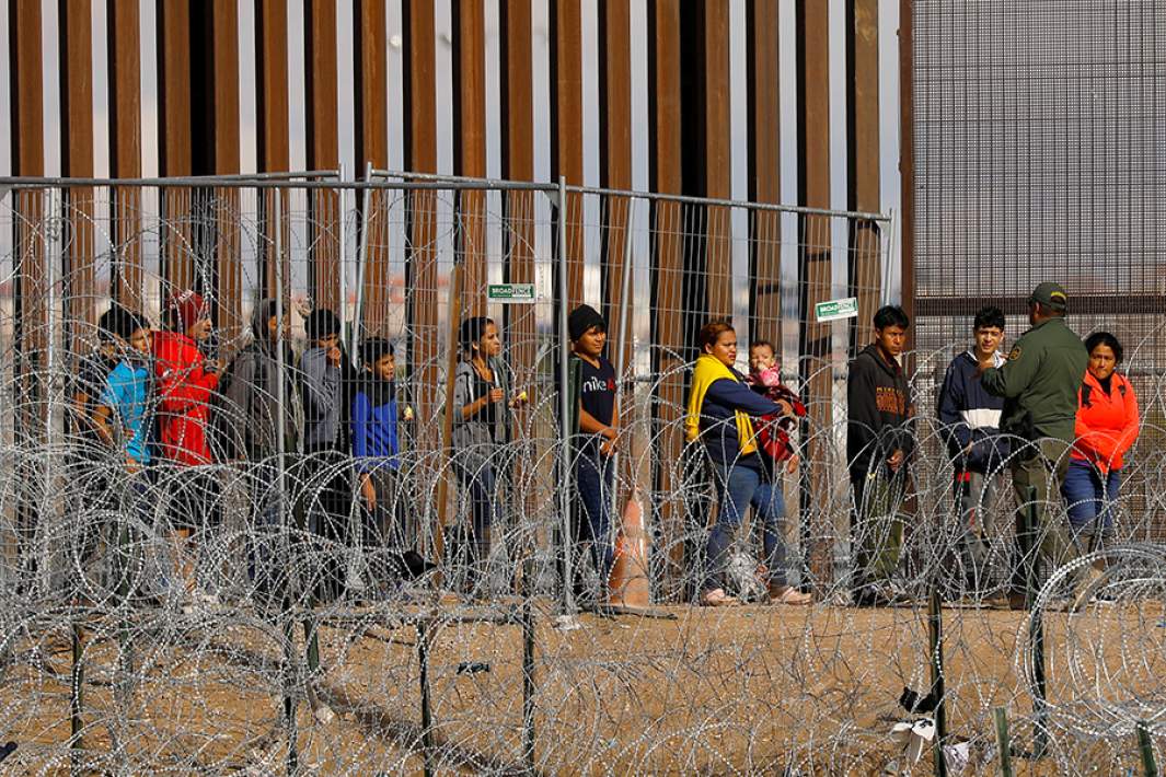Мигранты, ищущие убежища в США, собираются возле забора на границе США и Мексики, ожидая проверки пограничным патрулем США в Эль-Пасо, штат Техас
