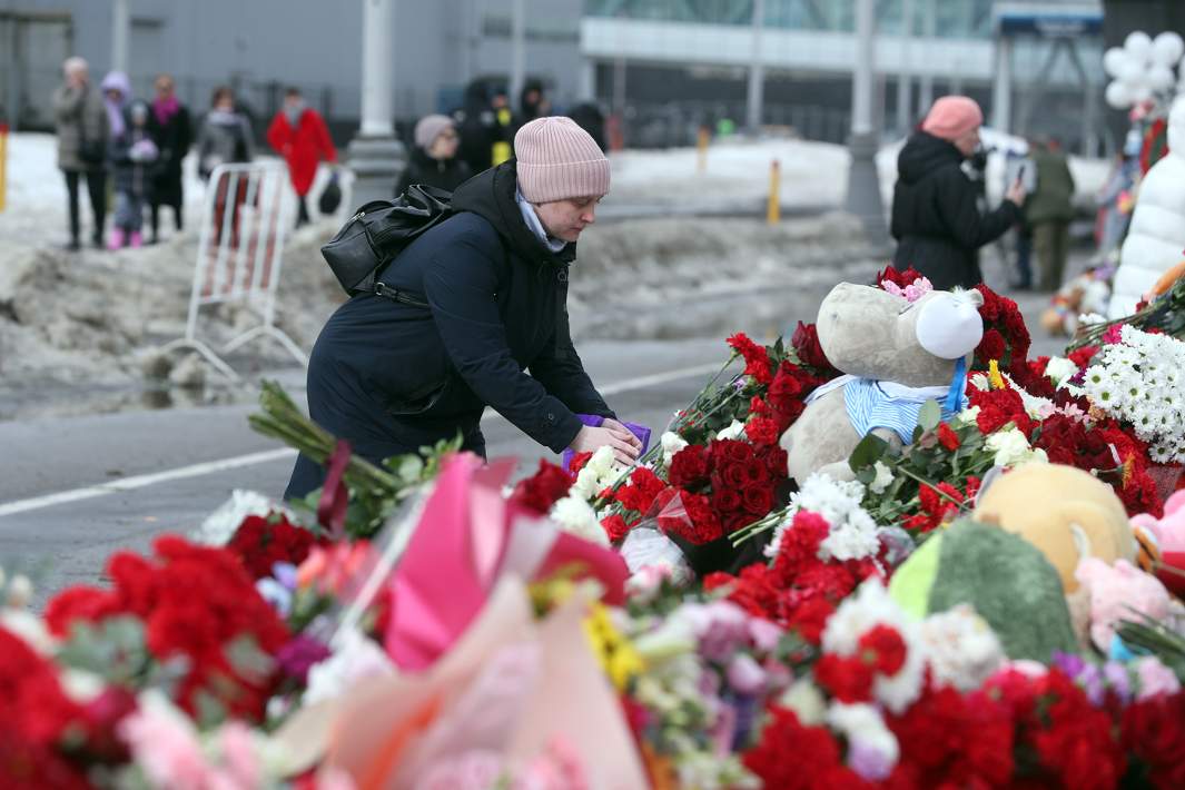 Женщина возлагает цветы у стихийного мемориала вдоль дороги у здания концертного зала «Крокус Сити Холл», где произошел теракт