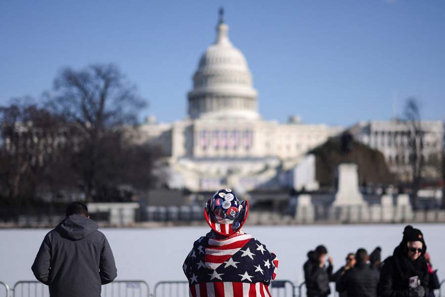 Люди стоят на фоне Капитолия США в день объявления о переносе инаугурации избранного президента США Дональда Трампа в закрытое помещение из-за опасно низких температур, ожидаемых в понедельник в Вашингтоне