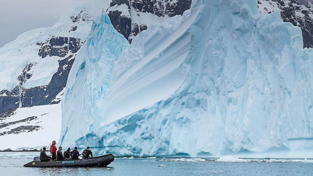 моторная лодка с аквалангистами проходит мимо айсберга 