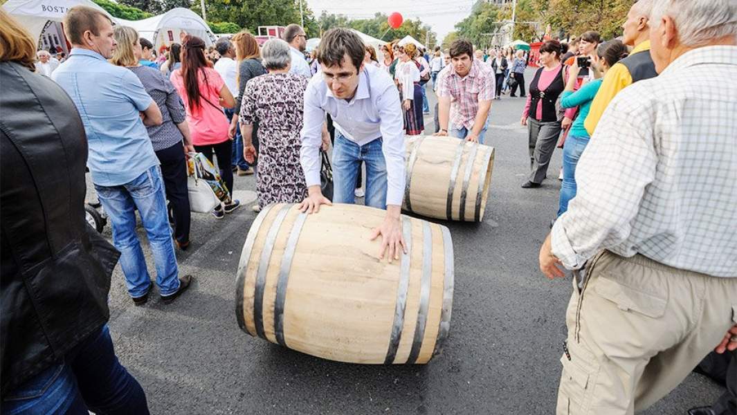 мужчины катят бочки с вином среди толпы во время Дня вина в Кишиневе