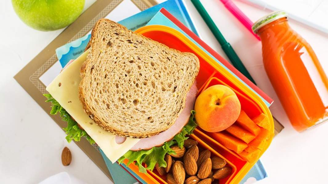 сэндвич с сыром, мясом и салатом, персик, миндаль и кусочки моркови в коробке для завтрака