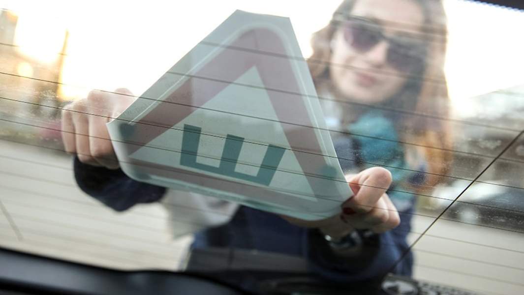 Водитель наклеивает предупреждающий знак «Шипы» на заднее стекло своего автомобиля