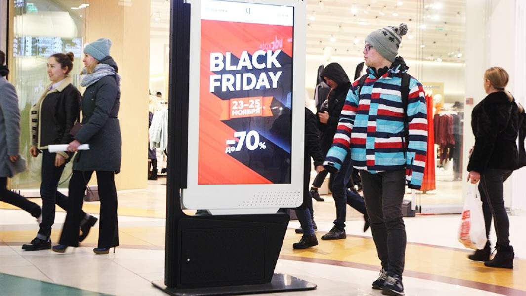 Покупатели в торговом центре у афиши со скидками