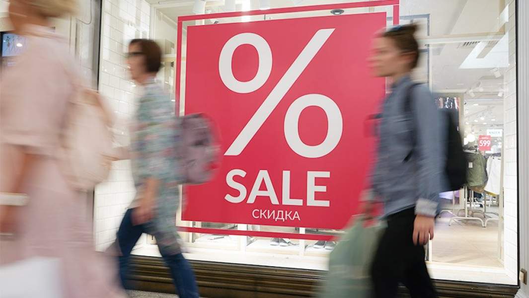 Люди проходят витрины с ообщением о скидках в магазине