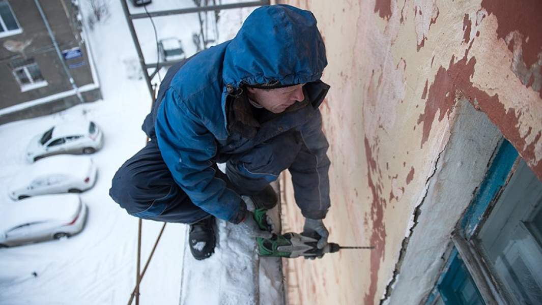Рабочий регионального фонда капитального ремонта многоквартирных домов ремонтирует фасад жилого дома в Омске