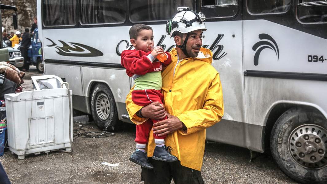 Член сирийской гражданской обороны «Белые каски» с ребенком на руках, деревня Калат аль-Мадик, к северу от Хамы, Сирия