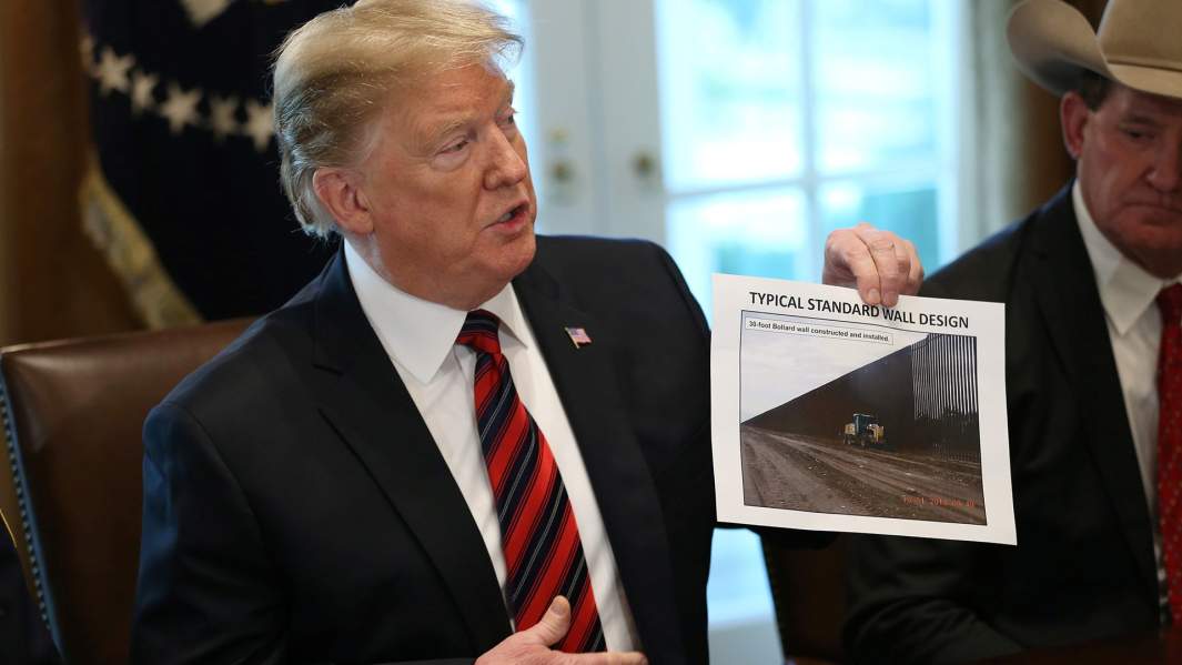 Президент США Дональд Трамп держит фотографию с изображением дизайна стены