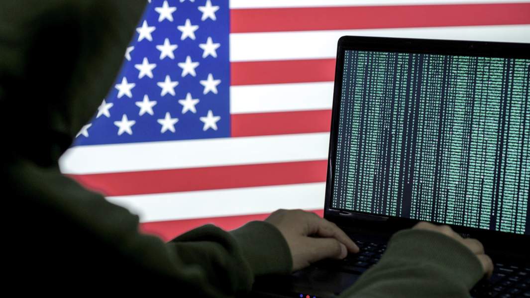 хакер за ноутбуком на фоне флага США