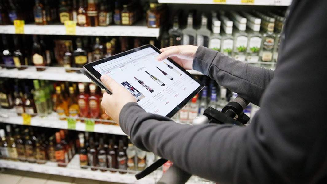 Человек выбирает вино в интернет-магазине, находясь в алкогольном отделе супермаркета