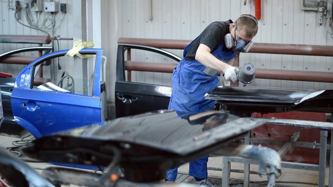 Сотрудник цеха кузовного ремонта наносит краску на поверхность детали автомобиля