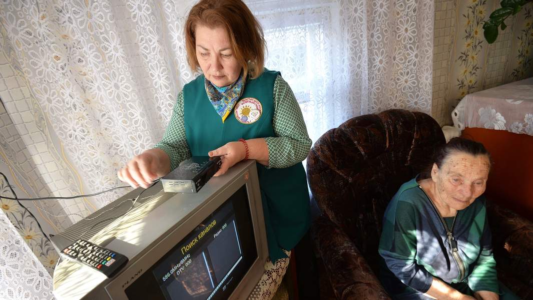 Волонтер (слева) помогает ветерану Великой Отечественной войны настроить прием цифрового телевидения