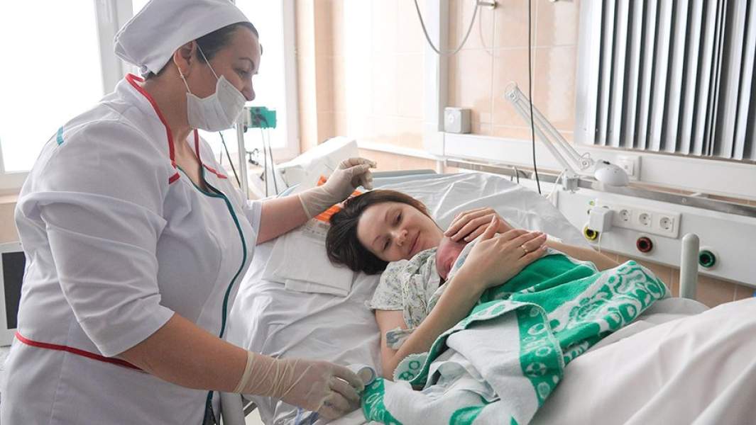 Врач и женщина с новорожденным ребенком в палате роддома в Москве