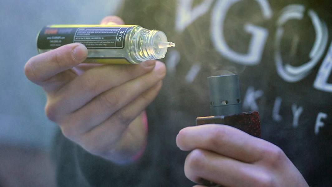 Мужчина заправляет вейп