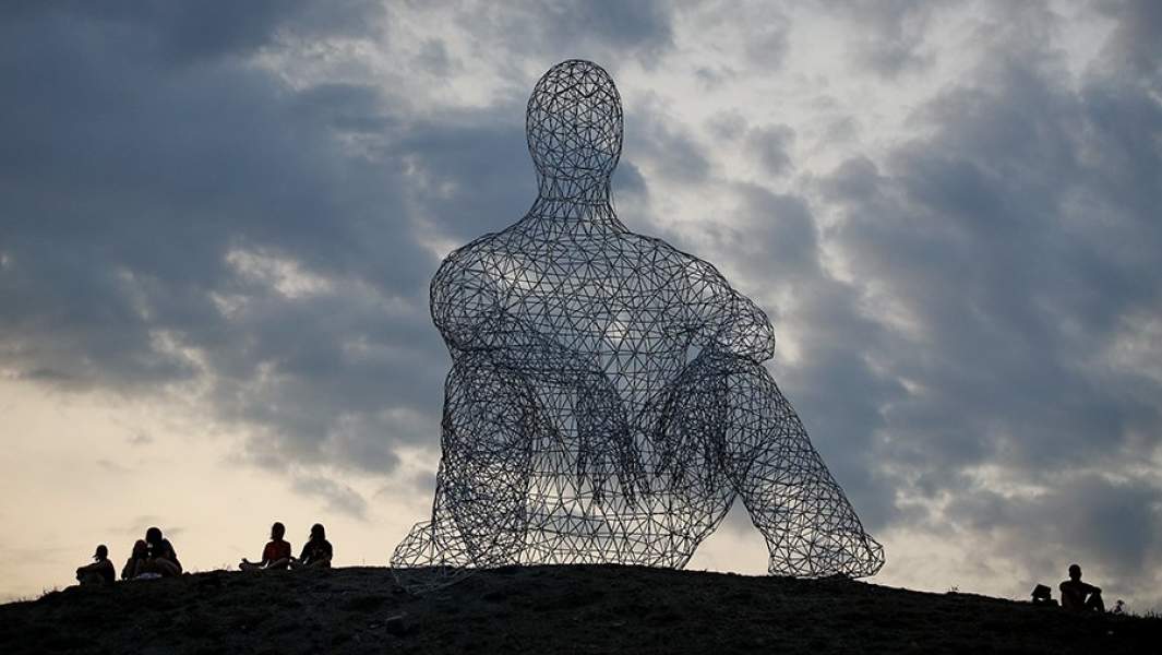 Скульптура огромного сидящего человека, собранная из нескольких тысяч металлических стержней