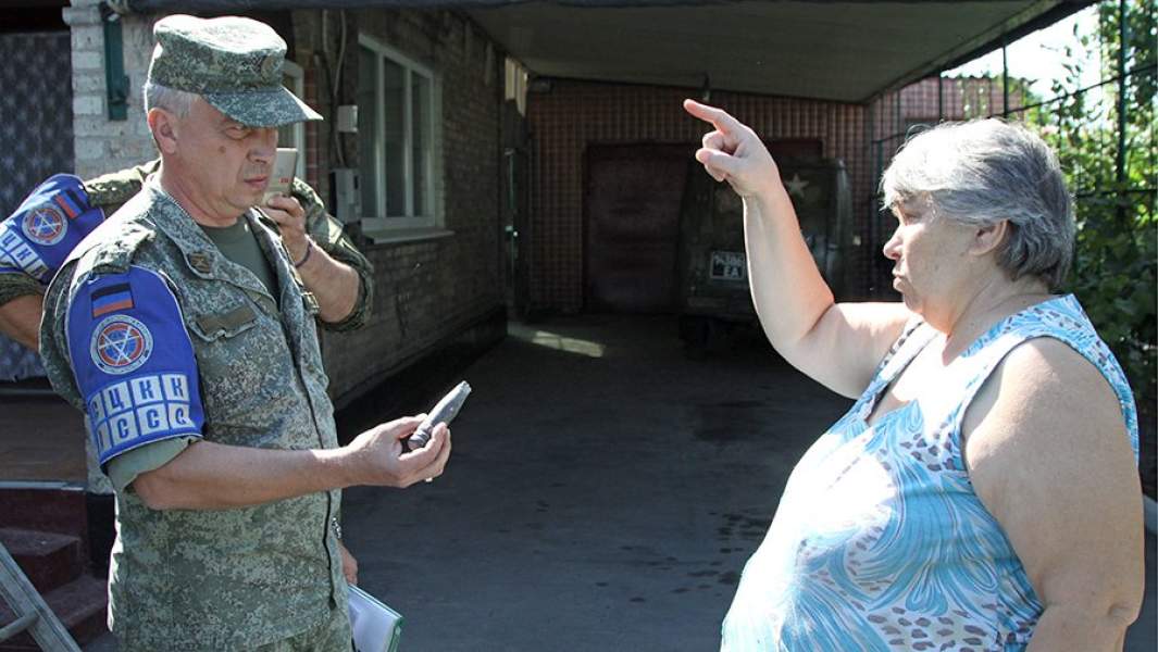 Офицер Совместного центра по контролю и координации режима прекращения огня ДНР опрашивает местную жительницу после ночного обстрела поселка Старомихайловка