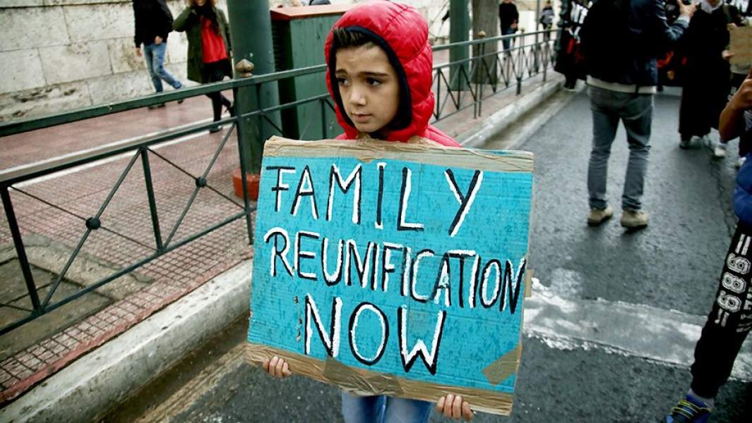 Маленький сирийский беженец держит табличку с надписью «Воссоединение семьям сейчас!» 