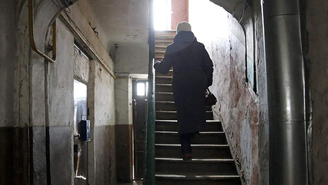 Жительница поднимается по лестнице в подъезде ветхого дома