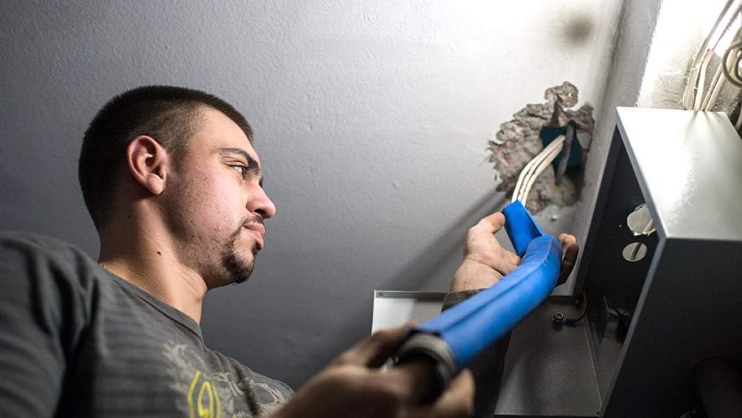 Рабочий меняет электропроводку в подъезде жилого дома