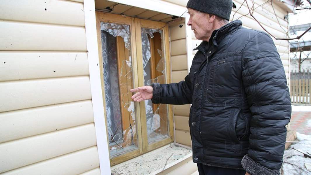Местный житель демонстрирует окно жилого дома, разбитое в результате артобстрела