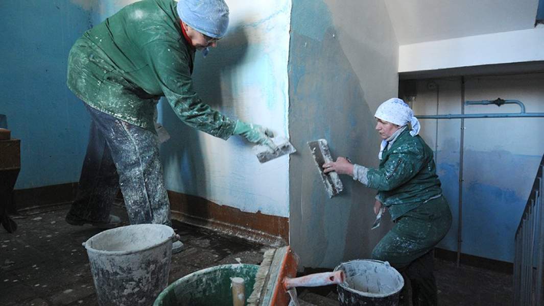 Маляры выравнивают стены во время ремонта лестничных пролетов подъезда жилого дома