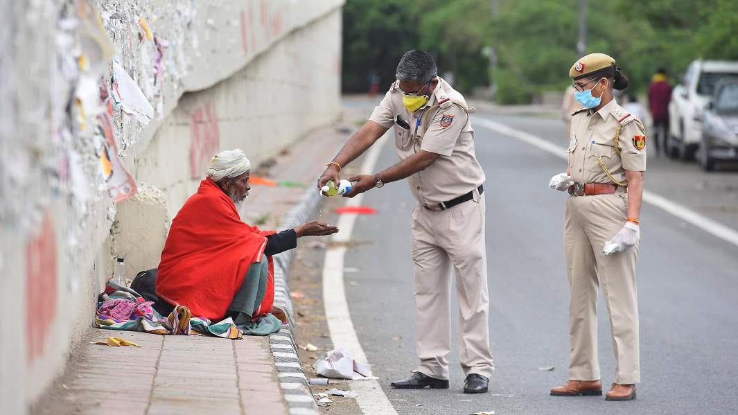 Сотрудники полиции Дели предлагают дезинфицирующее средство для рук бездомному человеку