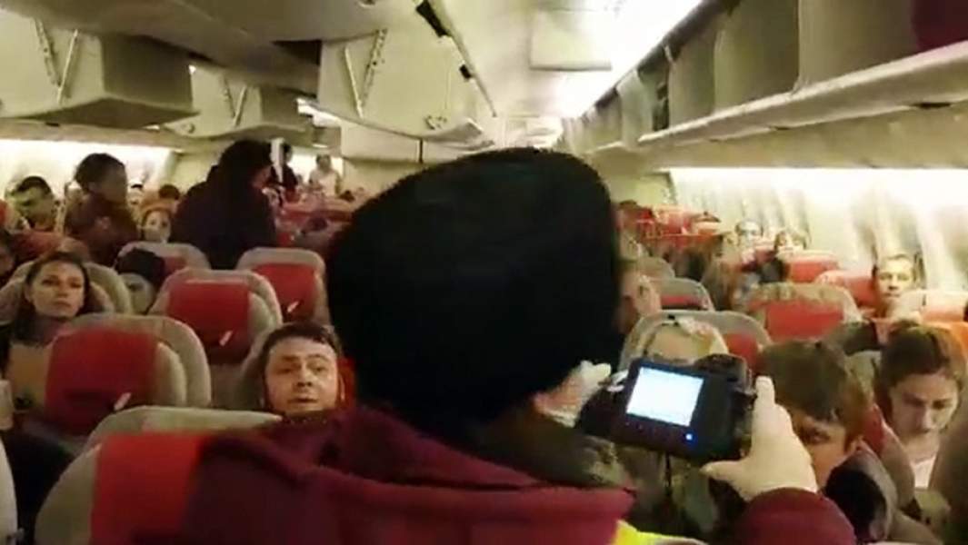 Сотрудник Роспотребнадзора дистанционно проверяет переносным тепловизором температуру пассажиров в самолете аэропорта Шереметьево