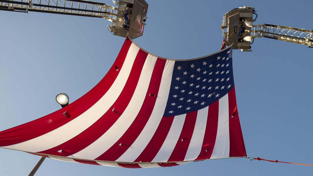 Пожарные поднимают огромный американский флаг, чтобы приветствовать героев с линии фронта пандемии COVID-19 в больнице Университета Северного побережья