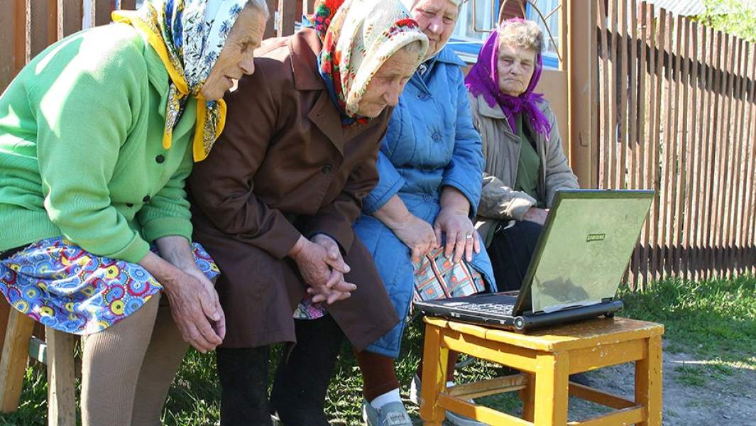 Пенсионерки рассматривают ноутбук во дворе сельского дома