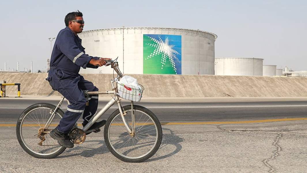 Рабочий проезжает на велосипеде мимо резервуаров на территории нефтеперерабатывающего завода компании Saudi Aramco на месторождении Абкаик в Саудовской Аравии