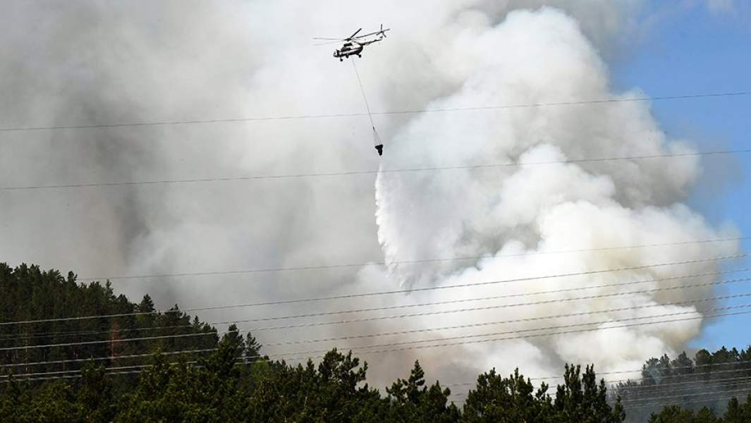 Вертолет Ми-8МБ МЧС России сбрасывает воду для тушения лесного пожара в тайге, угрожающего жилым домам в Красноярском крае