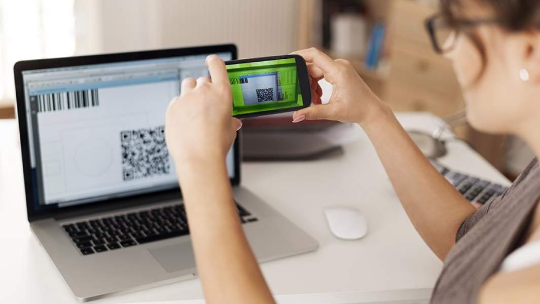 Девушка со смартфоном сканирует QR-код с экрана монитора