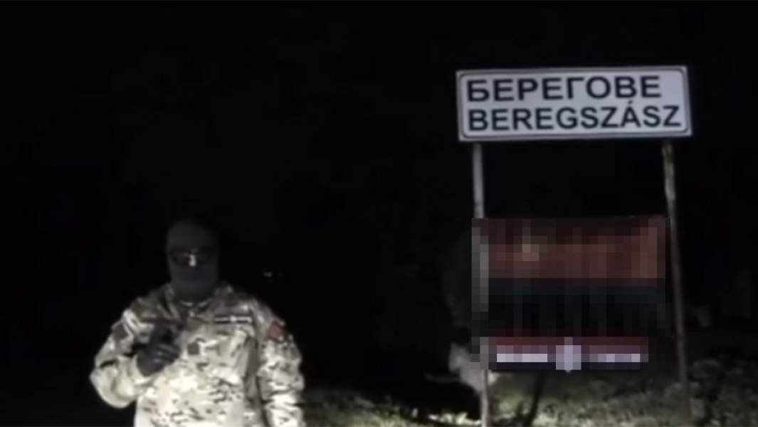 Мужчина в камуфляже и балаклаве на фоне флага «Правого сектора» (запрещен в России) угрожает венграм