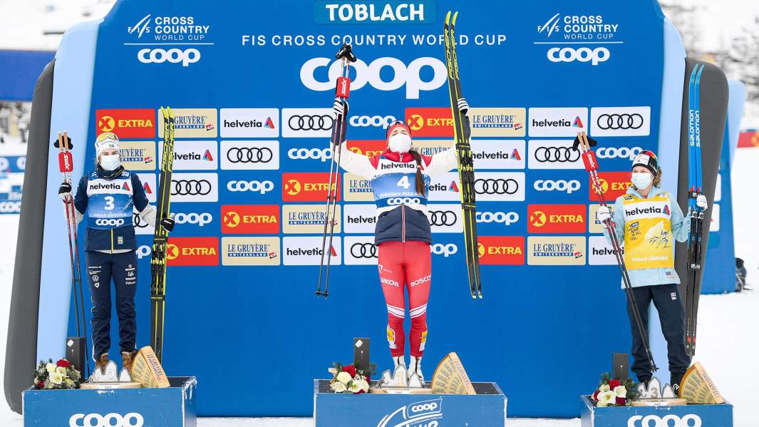 Эбба Андерссон из Швеции, Юлия Ступак из России и Джесси Диггинс из США на пьедестале почета после женской гонки преследования на 10 км классической техникой, Тоблах 