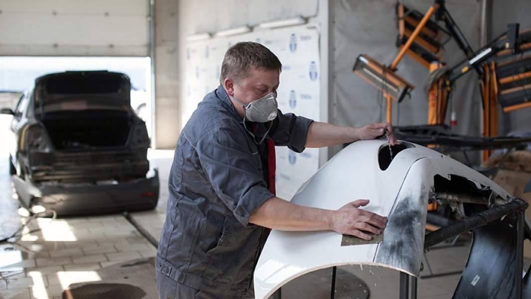 Сотрудник подготавливает запчасть автомобиля к покраске 