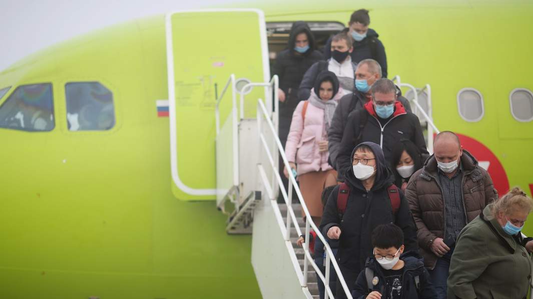 пассажиры в масках выходят из самолета