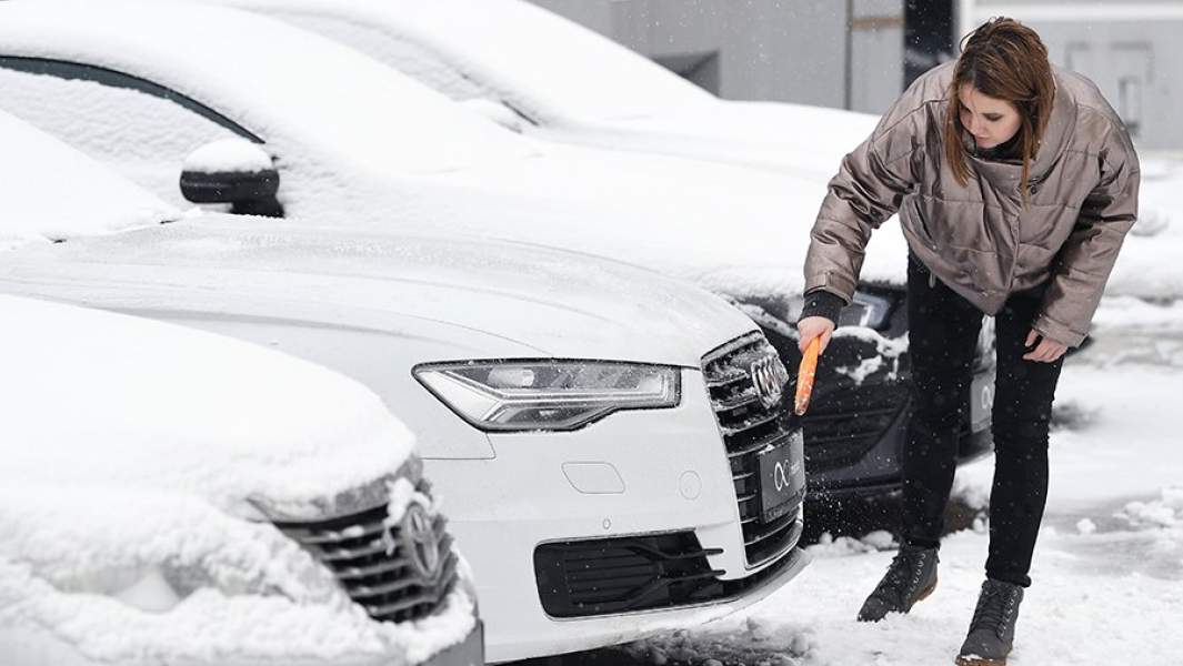 Девушка чистит автомобиль от снега на стоянке автосалона по продаже подержанных авто 