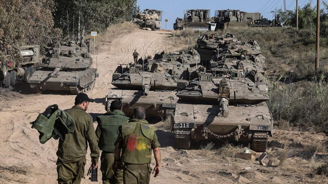 Израильские солдаты ходят вокруг танков в поле недалеко от границы между Израилем и сектором Газа