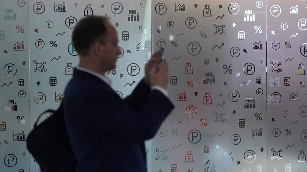 Мужчина на фоне стены с логотипом рубля