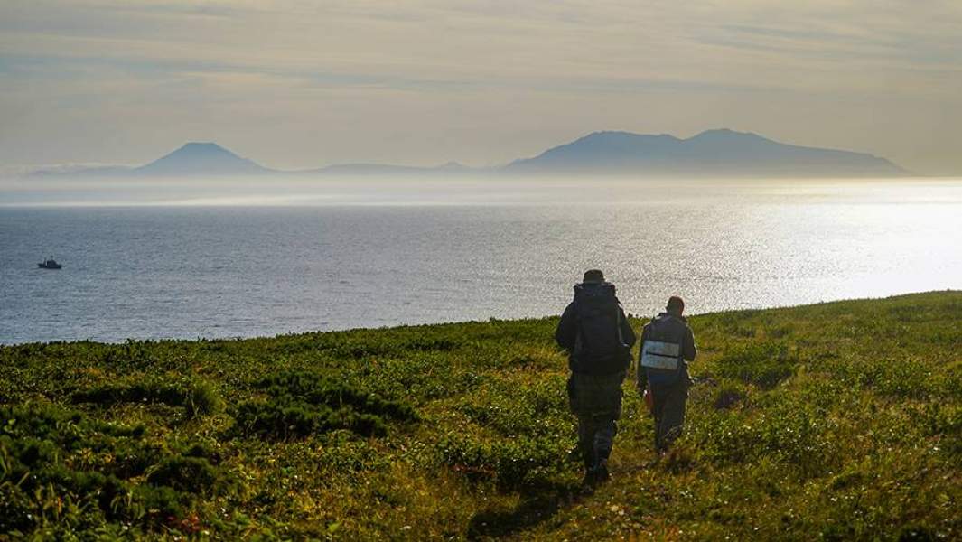 Туристы смотрят на пролив Фриза и остров Итуруп (на дальнем плане) с берега острова Уруп