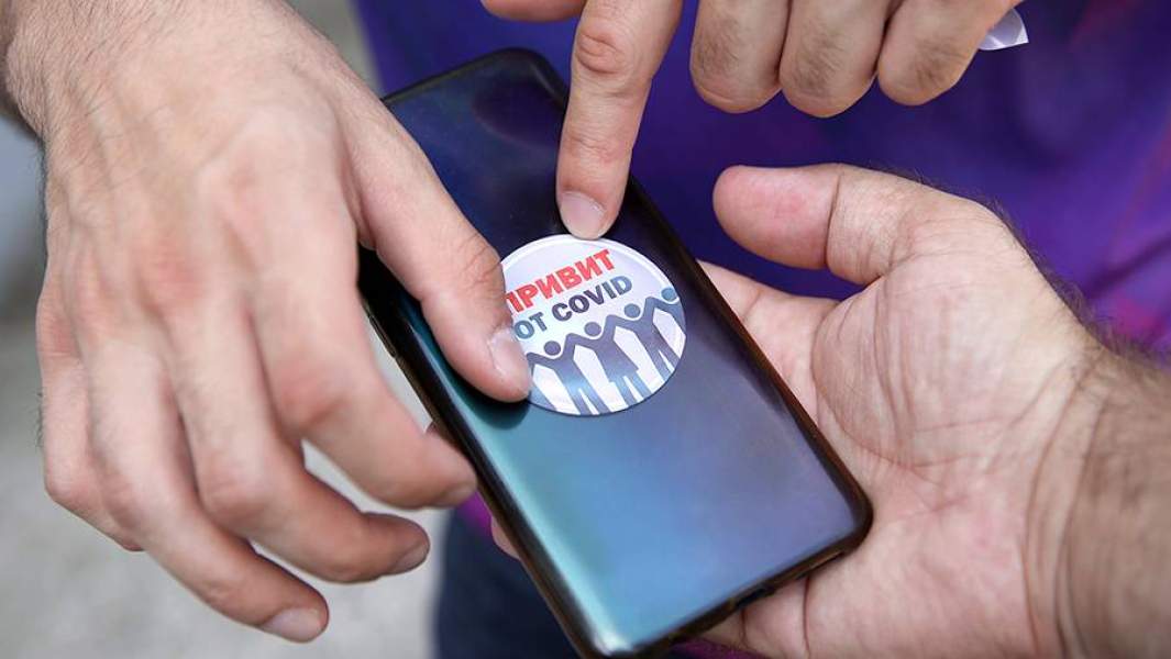 Наклейка с надписью «Привит от COVID» на смартфоне жителя, прошедшего вакцинацию от коронавируса в Краснодаре
