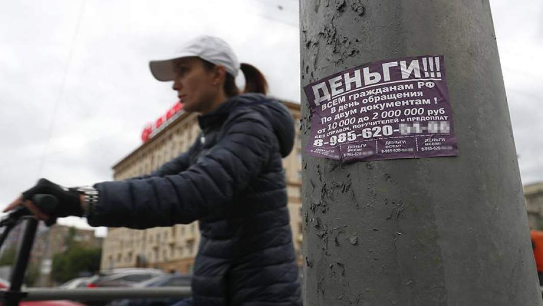 Женщина на самокате проезжает мимо столба с объявлением МФО