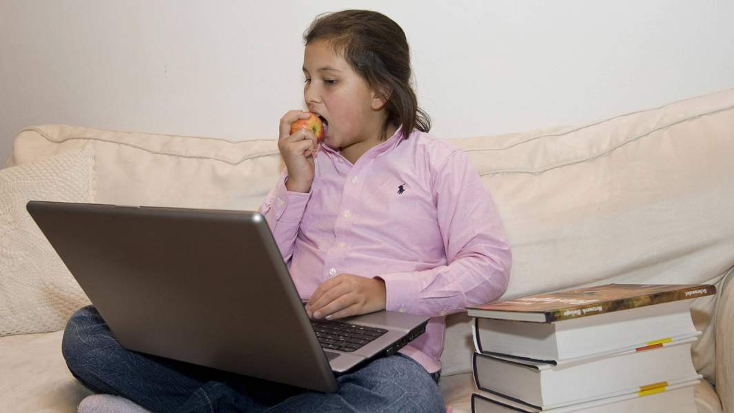девочка ест яблоко возле компьютера