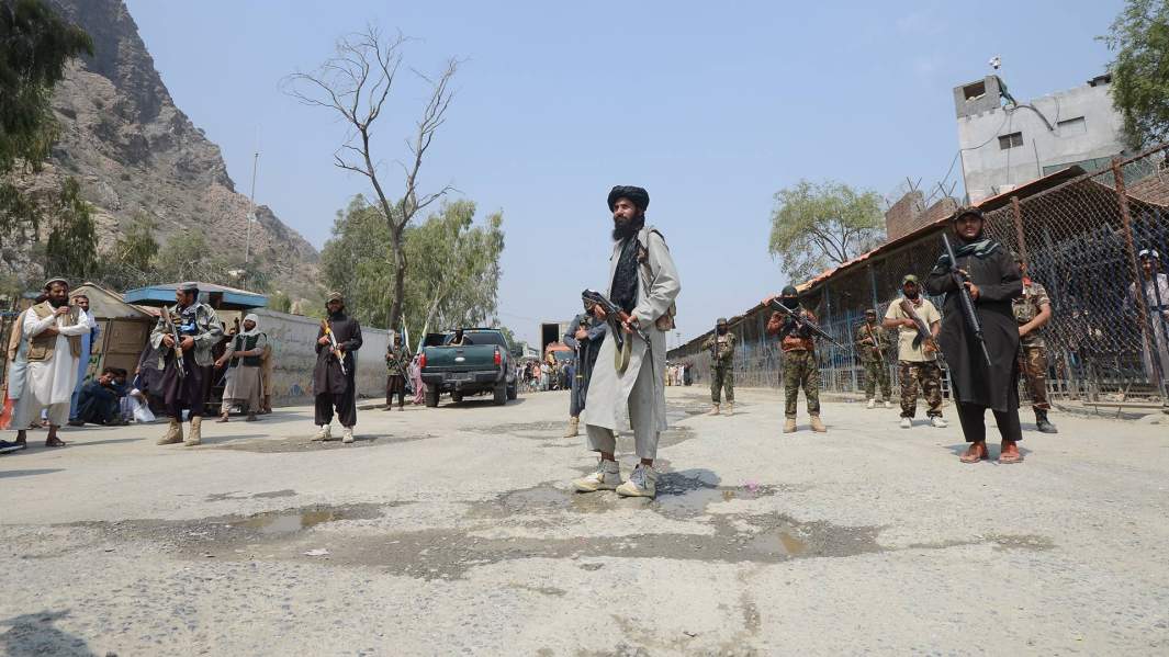 Пакистанский военизированный солдат (слева) и боевики Талибана охраняют свои стороны на пограничном переходе между Пакистаном и Афганистаном в Торкхаме, в районе Хайбер