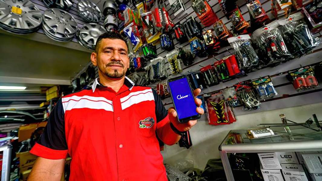 Продавец магазина автозапчастей показывает смартфон с приложением Chivo