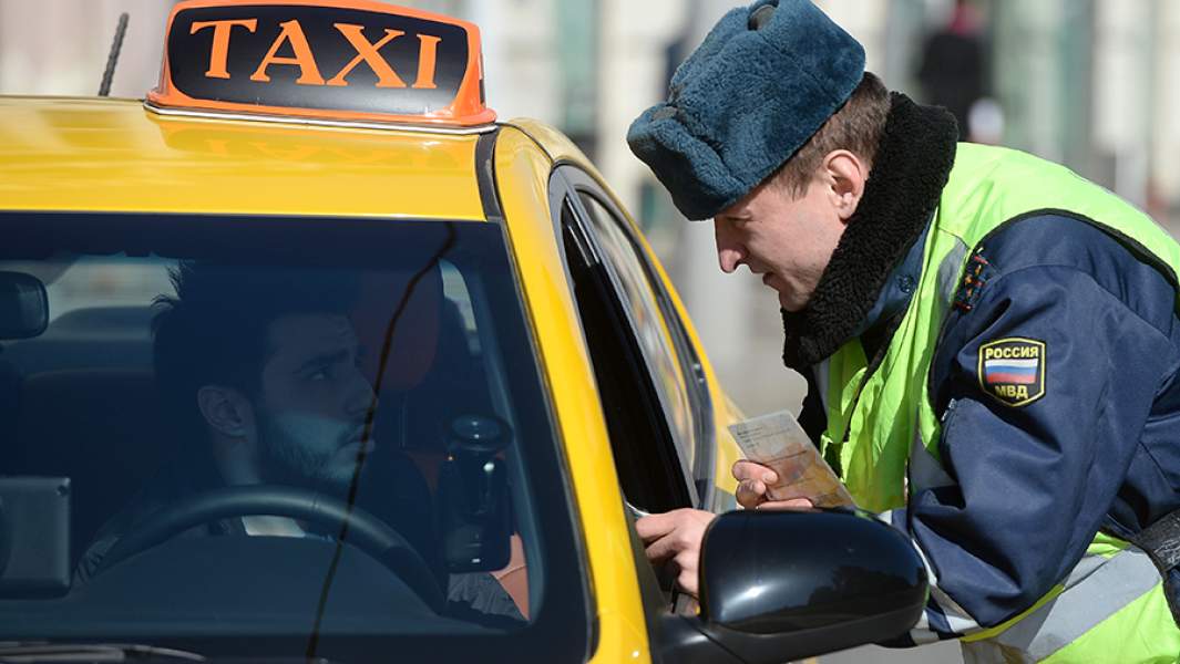 Сотрудник ГИБДД проверяет документы у водителя в рамках рейда против нелегальных таксистов в Москве