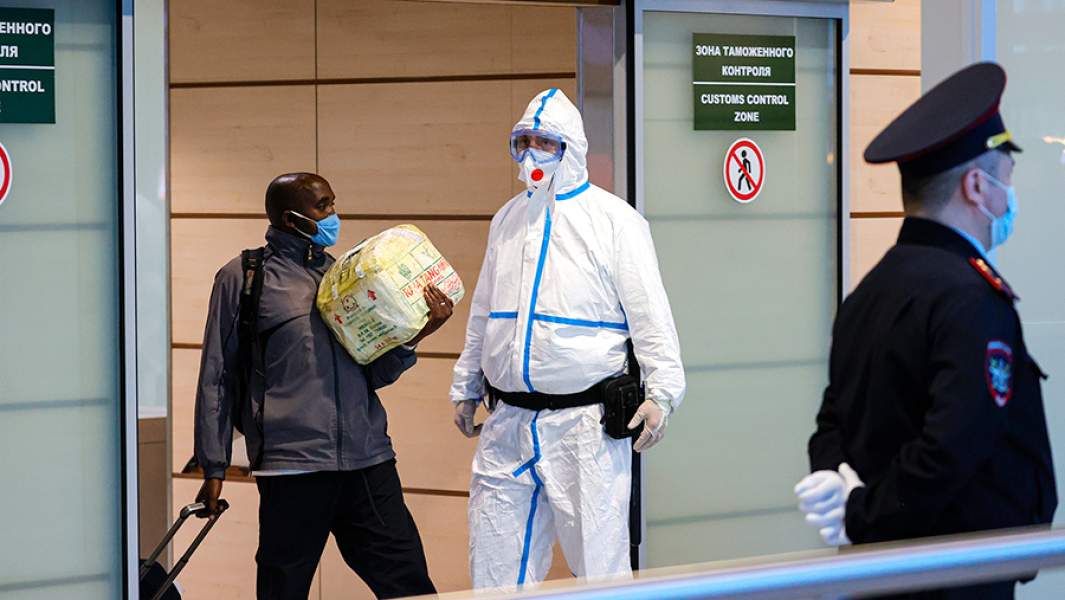 Турист, сотрудник аэропорта в защитном костюме и сотрудник полиции у зоны таможенного контроля в аэропорту Домодедово