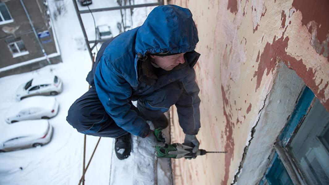 Рабочий регионального фонда капитального ремонта многоквартирных домов ремонтирует фасад жилого дома